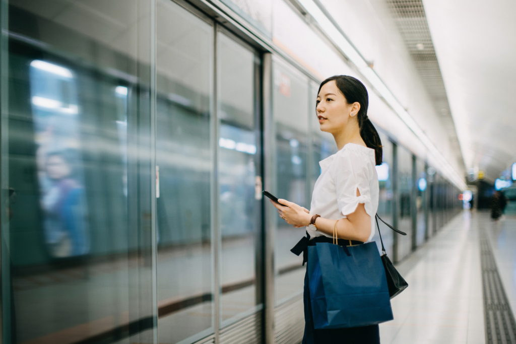 Young woman carrying shopping bag using smartphone while waiting for subway in platform